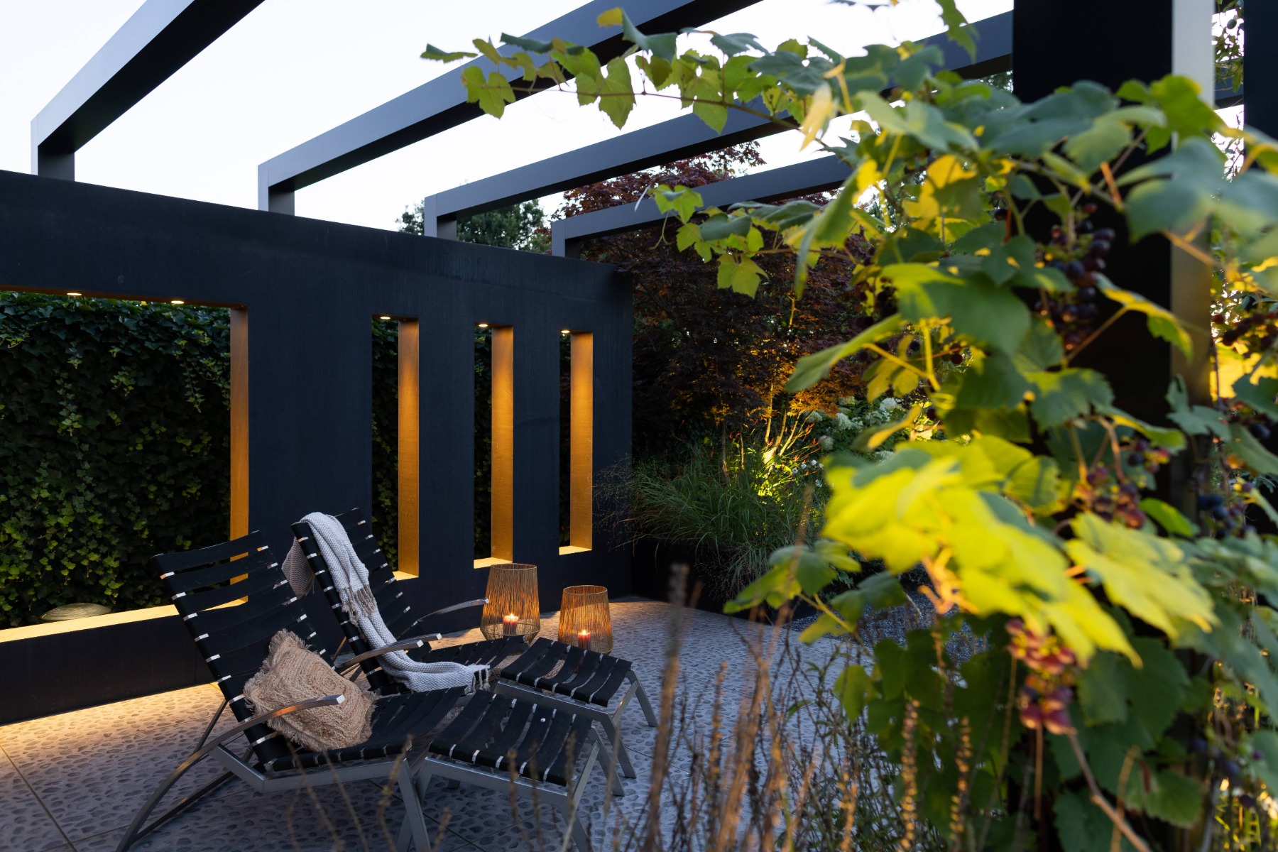 Ein moderner Sitzbereich mit Pergola wird von Deckenleuchten und Bodenleuchten, die in der Terrasse eingebaut sind, dekorativ beleuchtet.