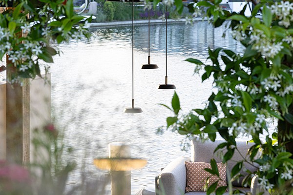 Dekorative Pendelleuchten, die außen als Beleuchtung unter einer Pergola angebracht wurden. Im Hintergrund sieht man Pflanzen und einen See.