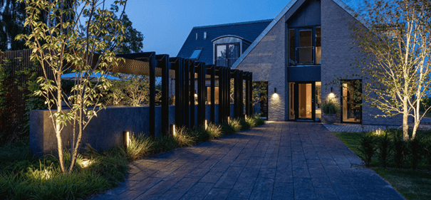 Dekorative Wegbeleuchtung vor einem Haus, die mithilfe von mehreren Pollerleuchten und Baumbeleuchtung gestaltet wurde.