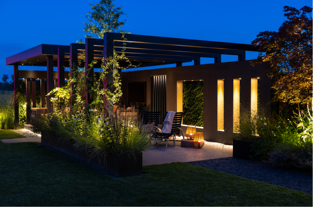 Eine Pergola wird von Aufbau-Deckenleuchten und Bodenspots von in-lite beleuchtet, sodass das Gerüst bei Nacht effektvoll hervortritt.